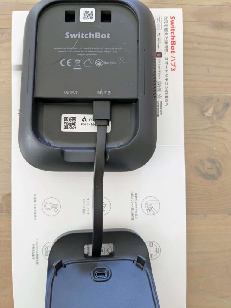 木目調床の上に置かれた、SwitchBot ハブ3本体背面と専用スタンド。付属ケーブルで接続された状態。
