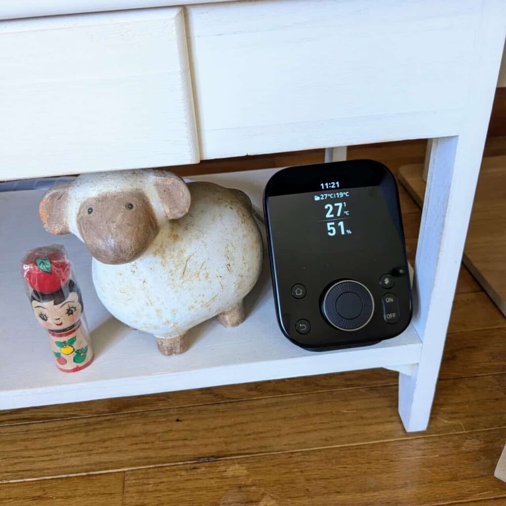 白い棚の段に設置されたSwitchBot ハブ3と、その横に並ぶ羊の置物およびこけし。